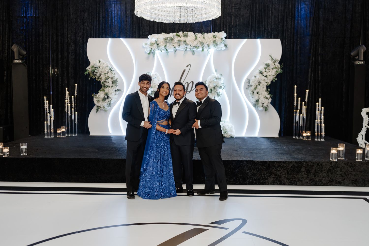 Elegant wedding reception with guests posing in front of a modern white and black backdrop with floral decor.