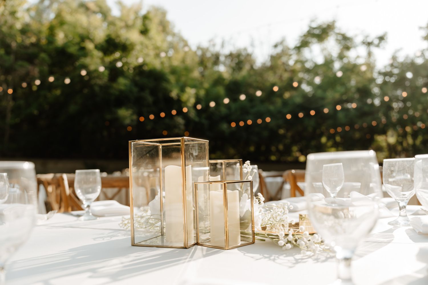 Wedding reception table settings with gold geometric centerpieces and string lights overhead.