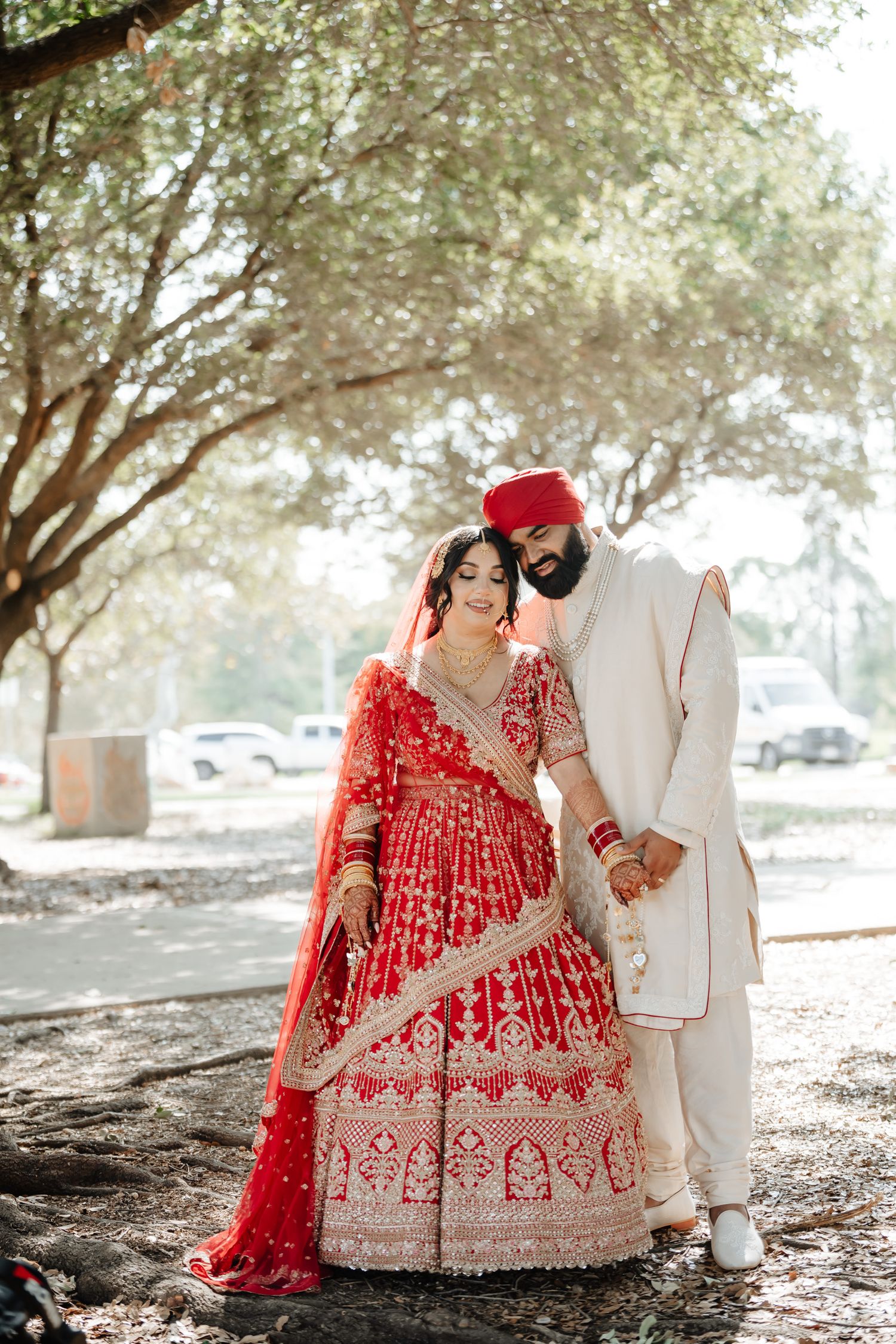 A romantic couple's photoshoot under trees featuring traditional Indian wedding attire and natural lighting.