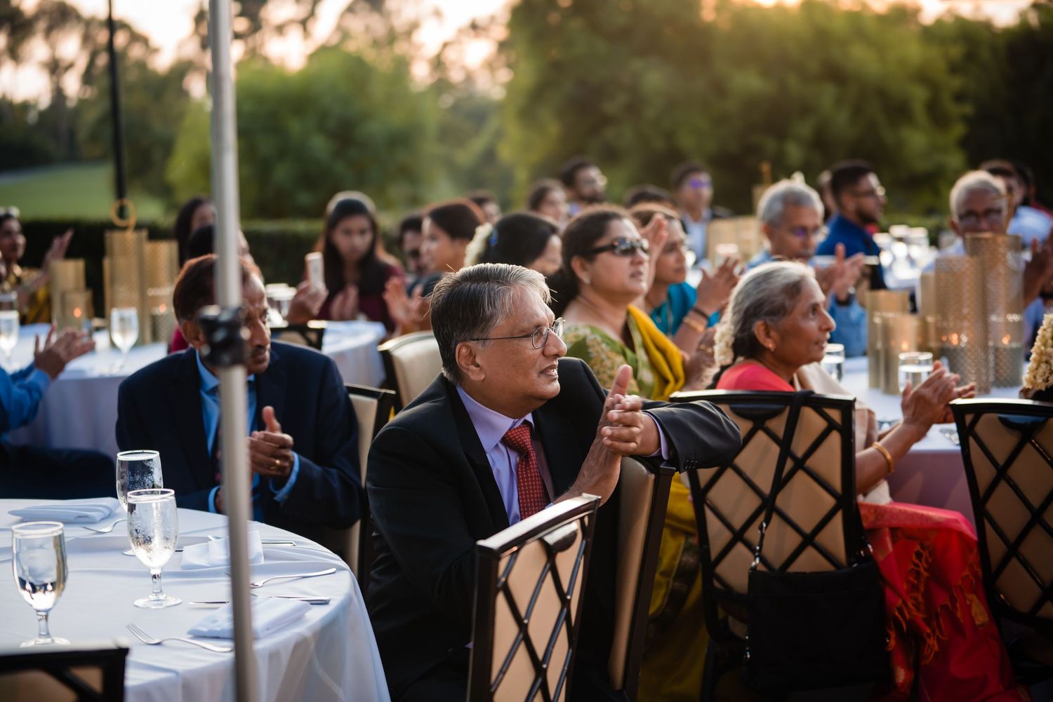 Guests mingle and socialize at an elegant outdoor evening reception with tables and chairs set up on a patio.
