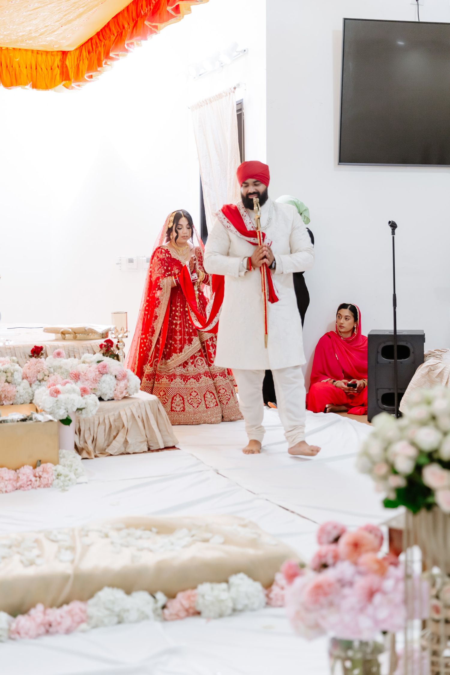 Traditional Sikh wedding ceremony with red and gold decor featuring floral arrangements and elegant seating.