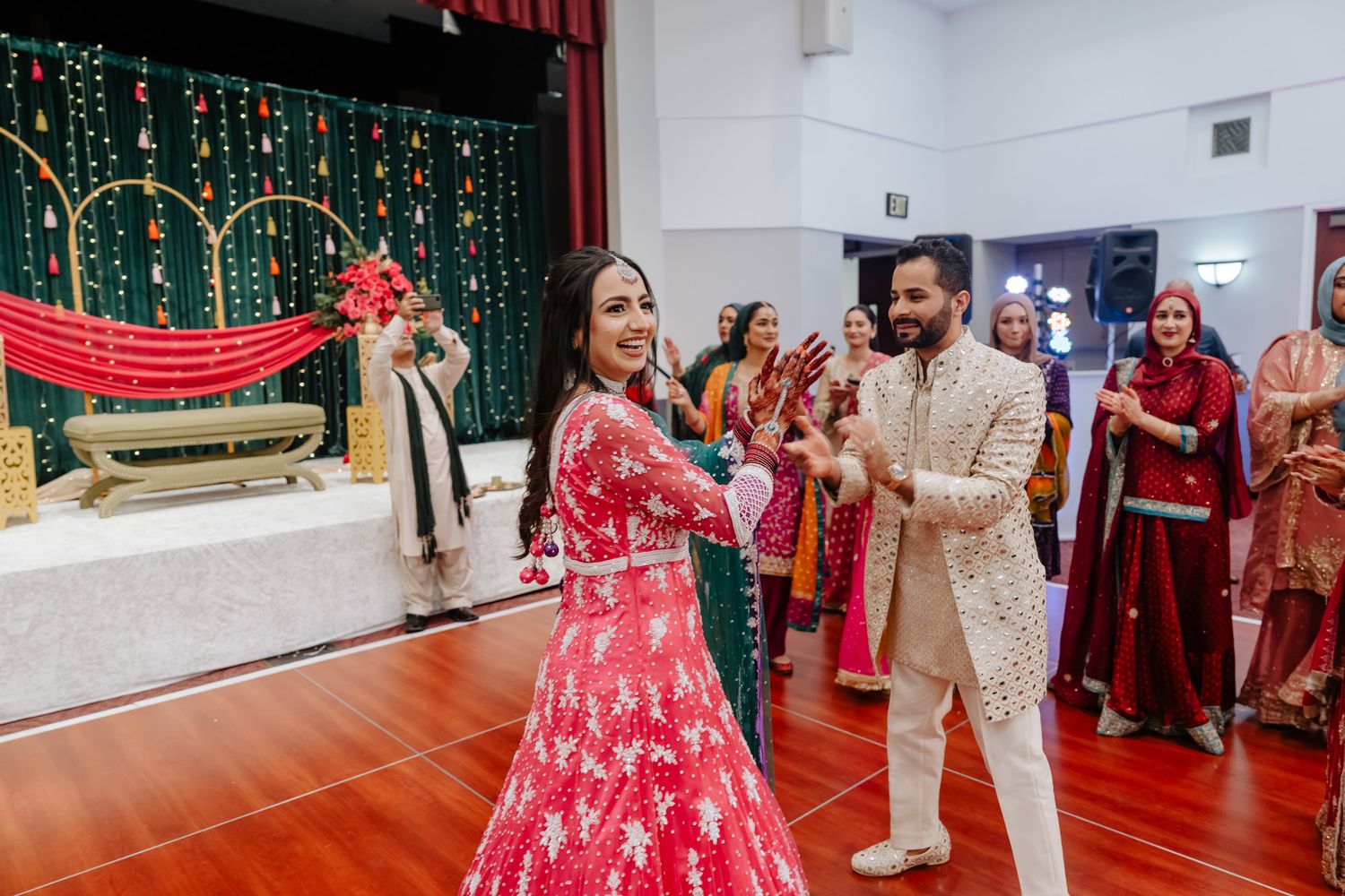 Wedding celebration in a banquet hall with string lights and decorative backdrop showing joyful dancing.