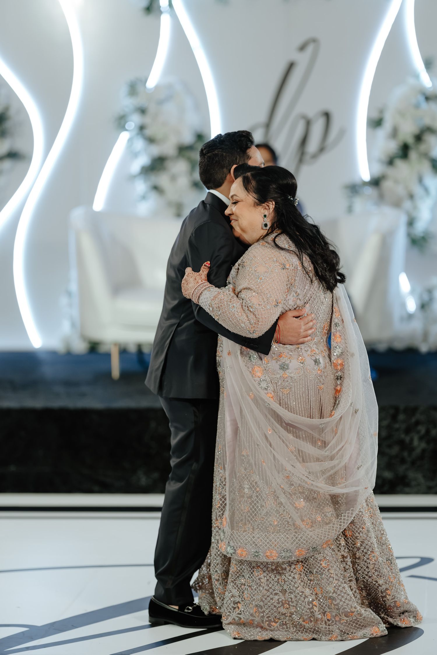 Couple sharing an intimate dance moment on a sleek white dance floor with illuminated backdrop.
