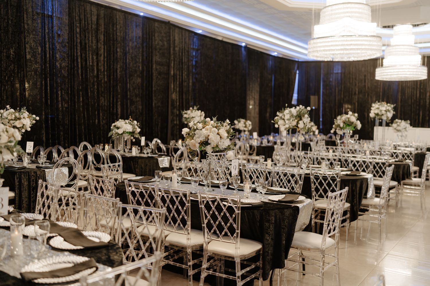 Modern wedding reception venue with elegant white table settings and crystal chandeliers.