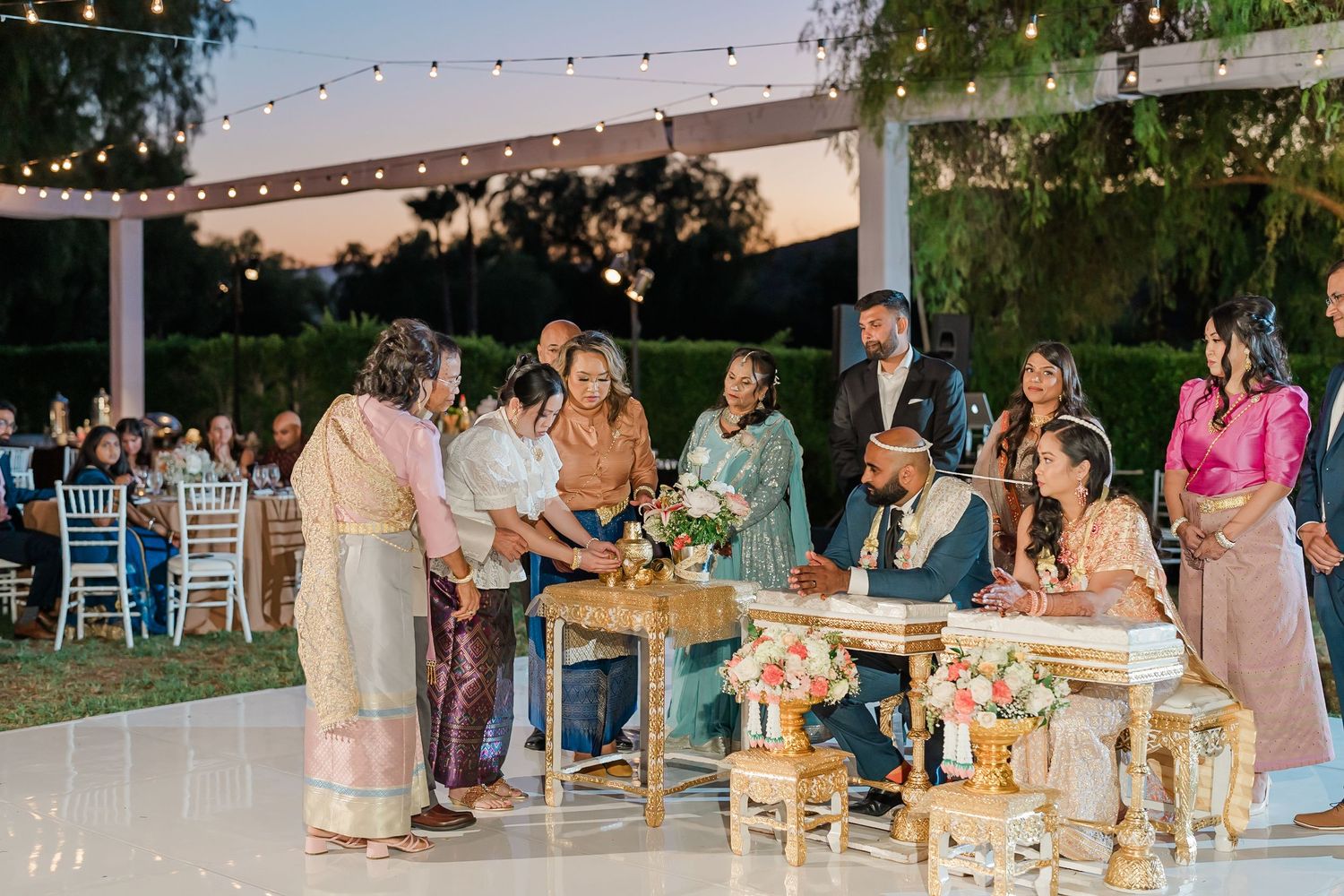 Outdoor wedding reception setup with string lights and guests mingling at dusk.