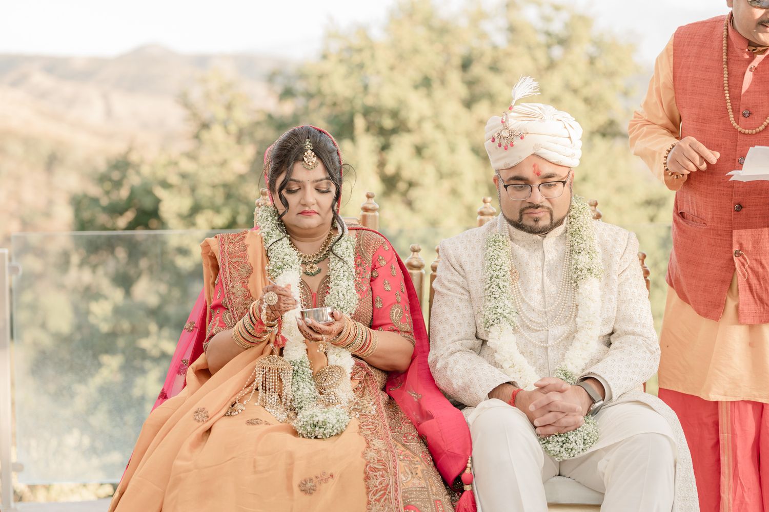 Traditional Indian wedding ceremony with guests gathered outdoors under elegant white and coral decor.