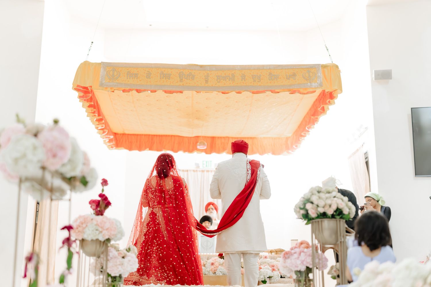 Indoor wedding ceremony space decorated with white floral arrangements and red accents.