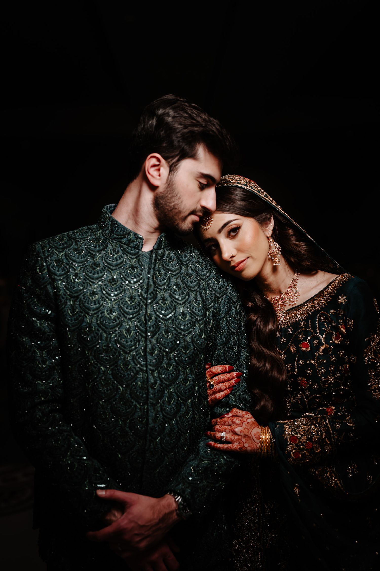 A romantic couple in dark attire embraces intimately against a black backdrop in a series of artistic wedding photos.