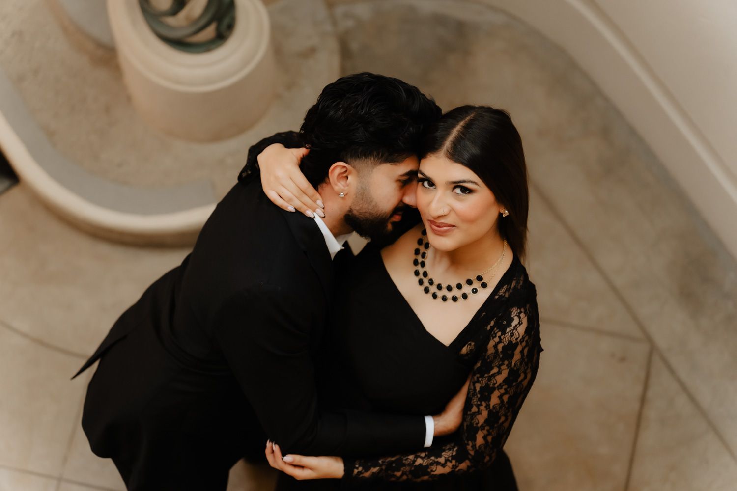 Romantic couple in black formal wear sharing an intimate moment, woman smiling joyfully.