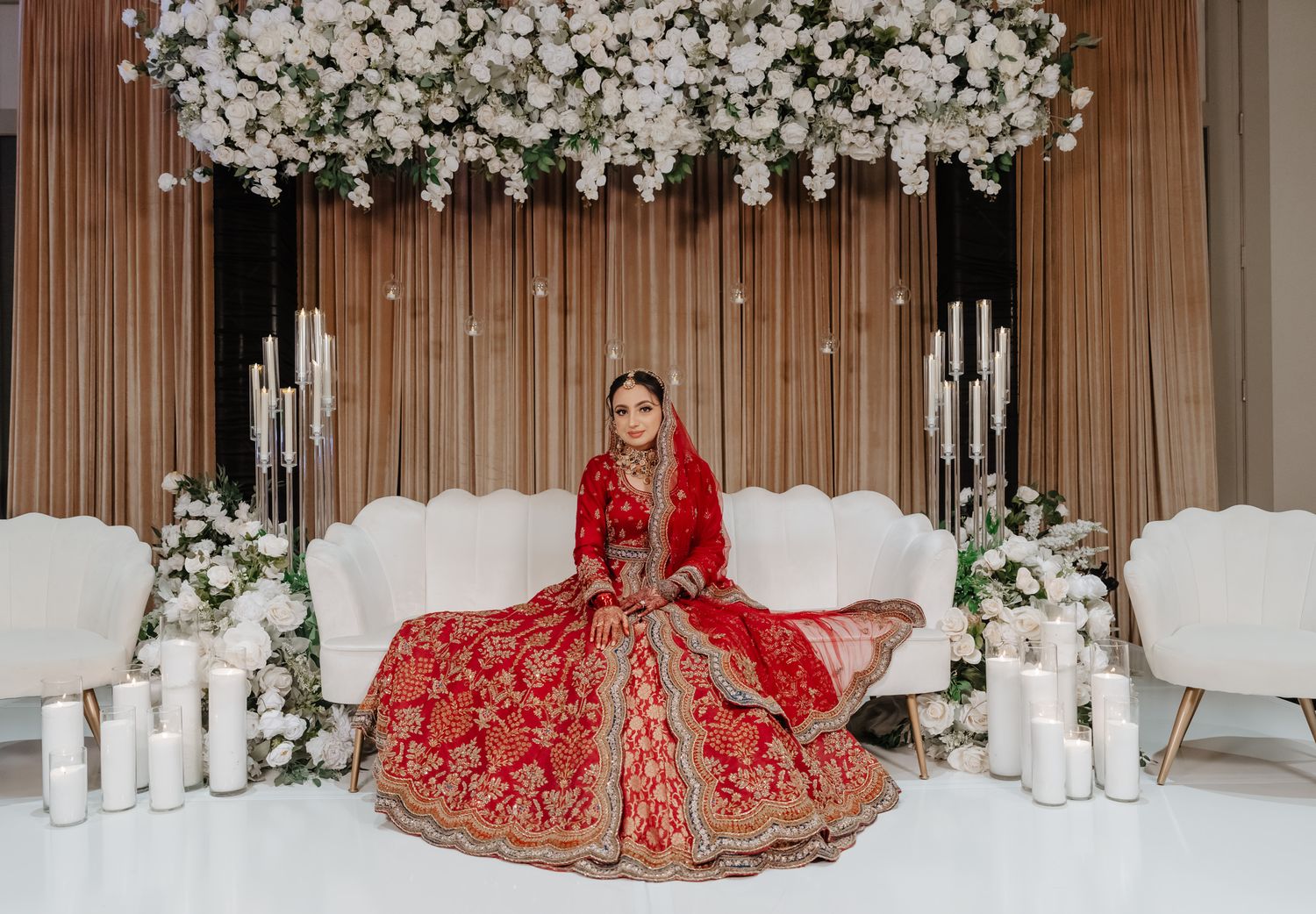 Wedding ceremony setup with white floral arch, candles, and traditional Indian bridal decor.