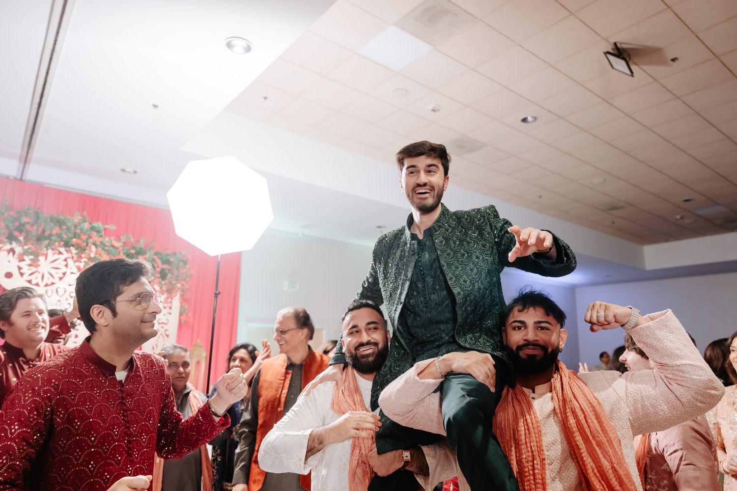 A group dances and celebrates at a vibrant Indian wedding reception with colorful traditional attire and decor.