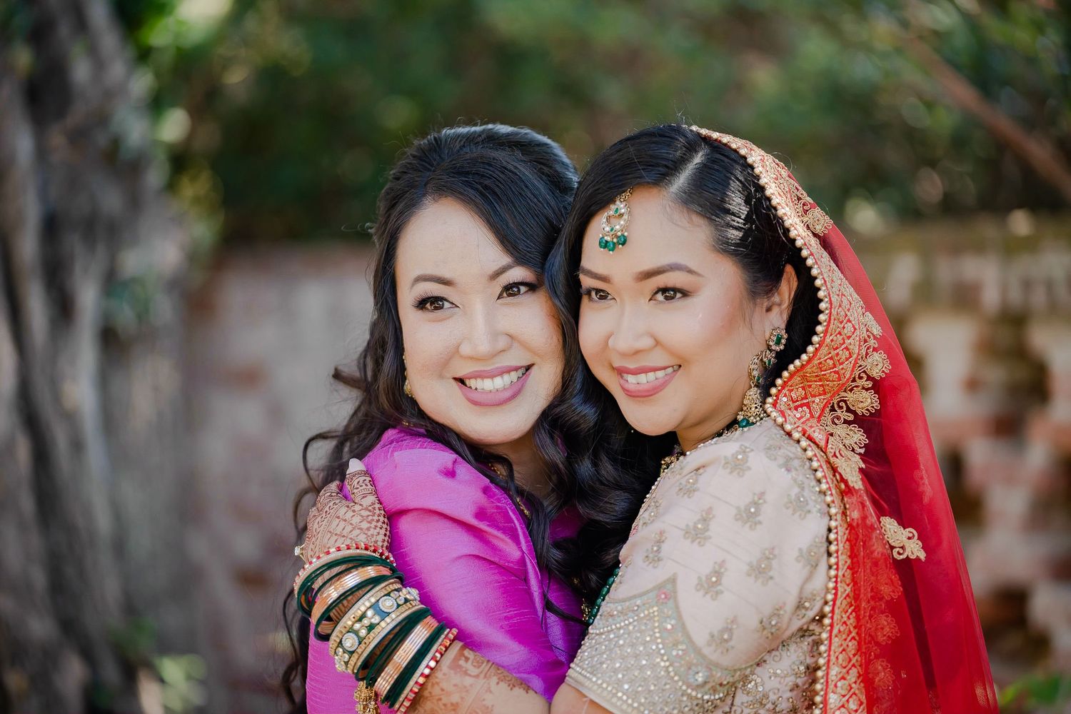 A bride in traditional Indian wedding attire poses with loved ones in a garden setting during a celebration.