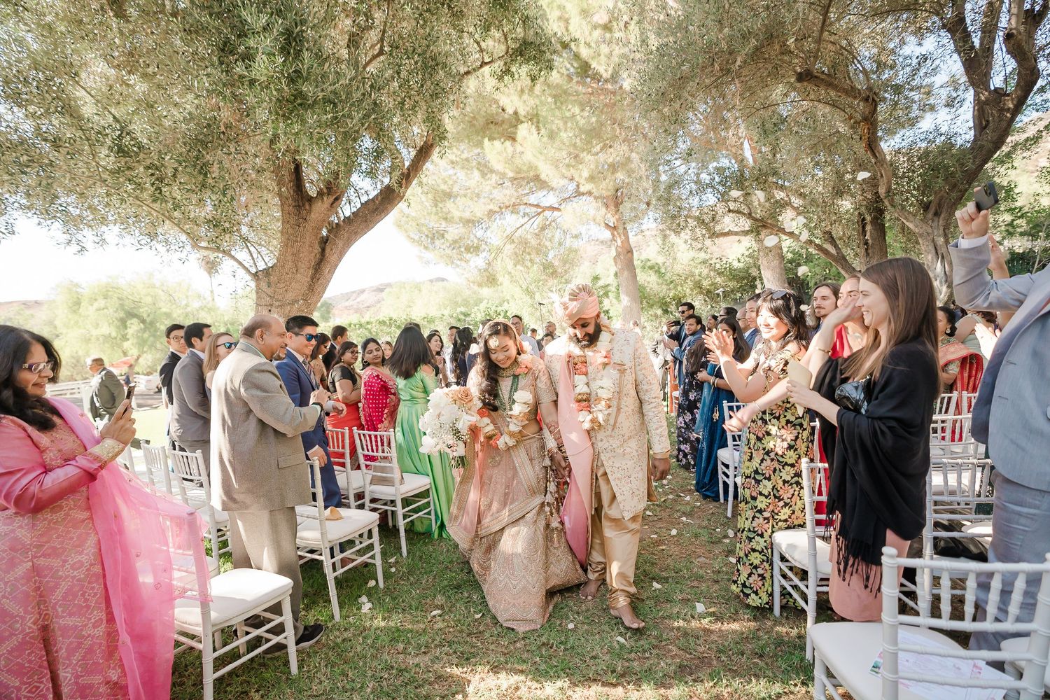 Outdoor wedding celebration with guests gathered under shady trees.