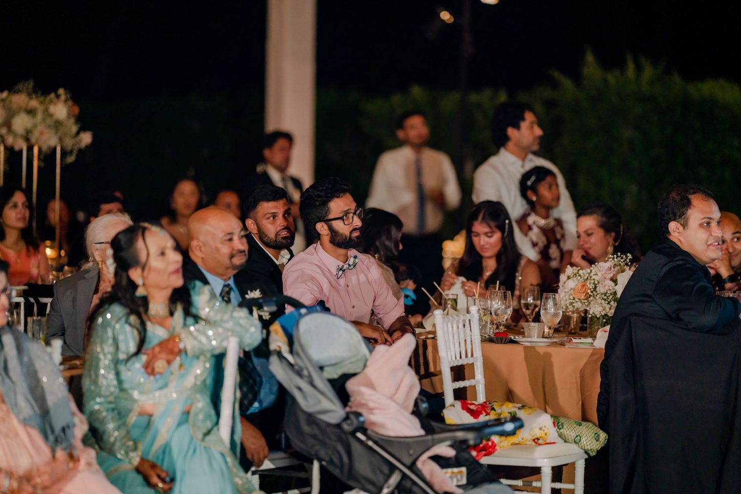 Wedding guests enjoy the evening reception while seated at decorated outdoor tables.
