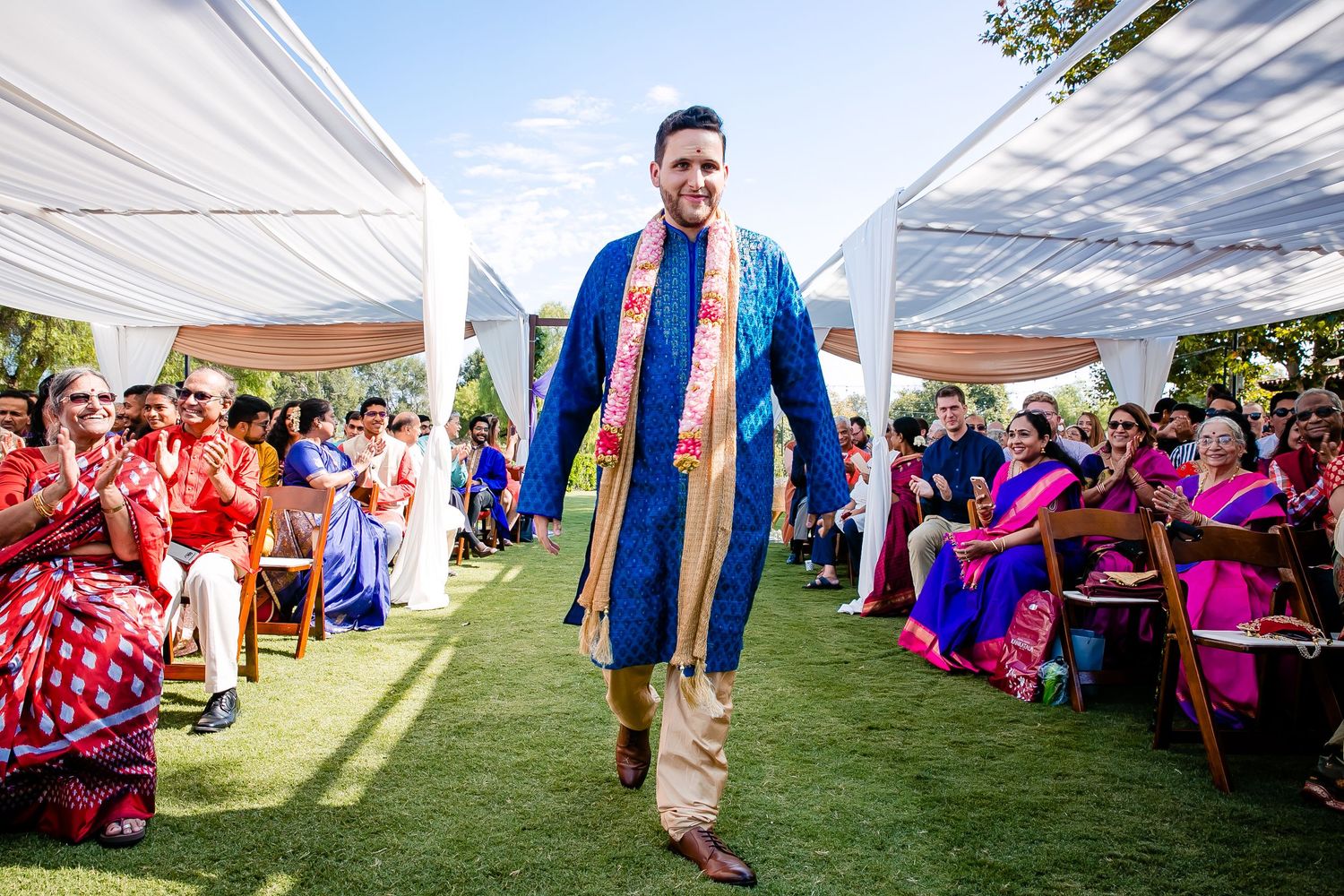 A festive outdoor wedding reception under white tents with guests seated at tables decorated in bright pink accents.