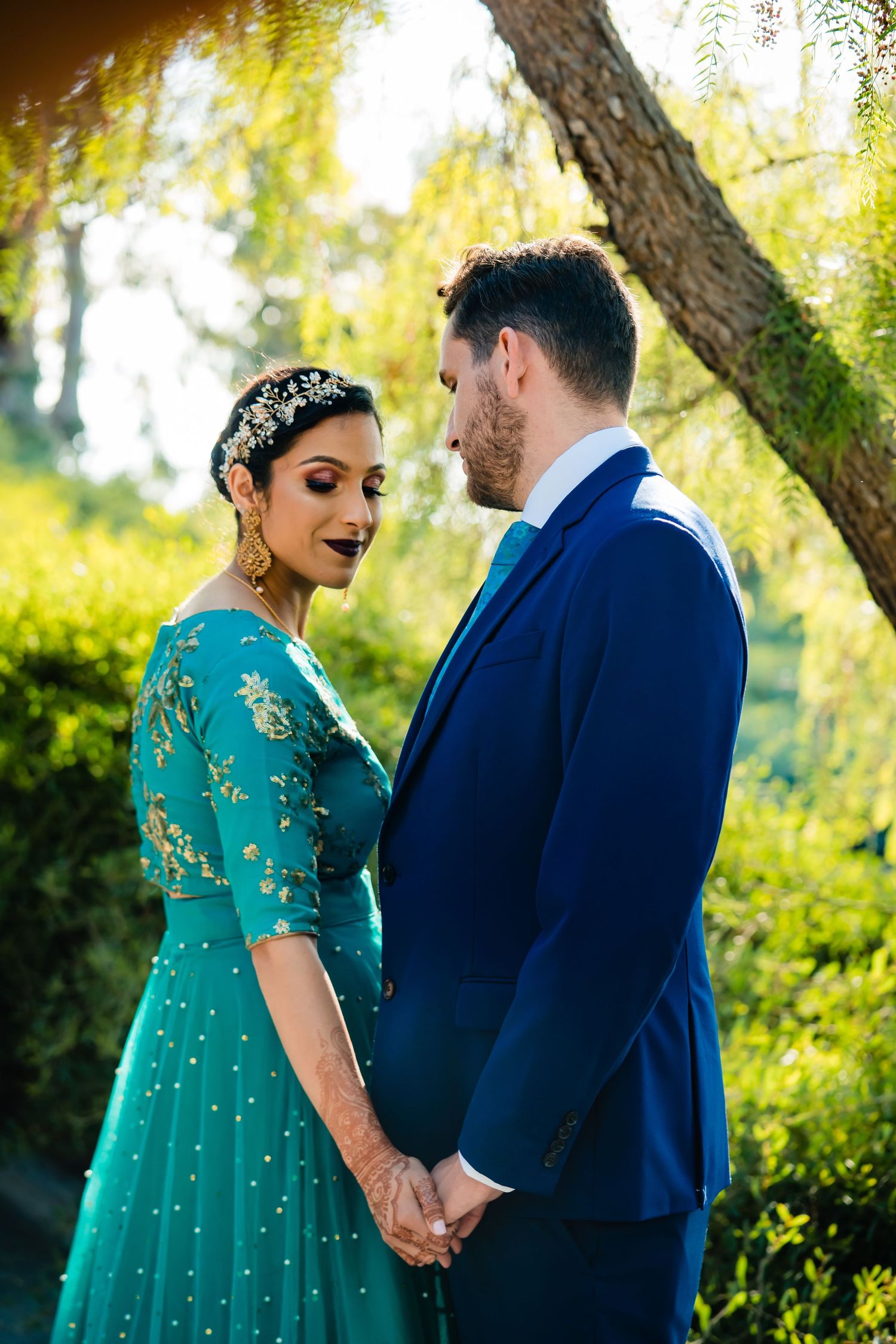 A couple in a navy suit and emerald green dress share joyful moments together in a sunlit garden setting.