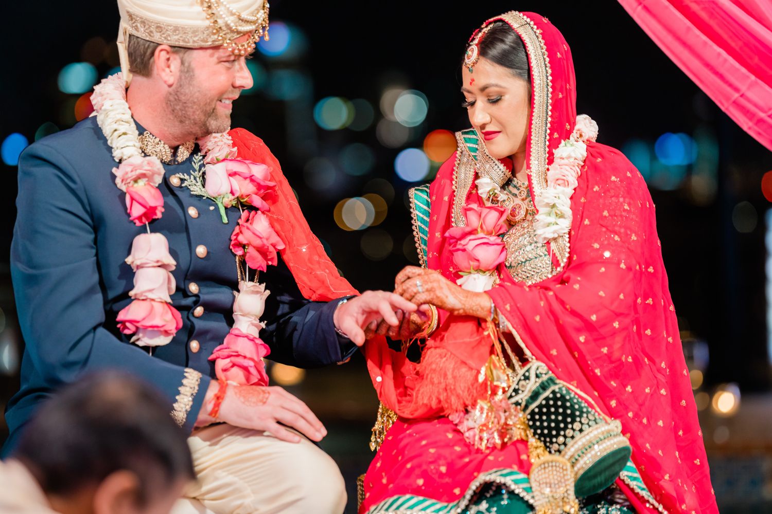 Wedding couple performs traditional ceremony rituals under red decorative canopy at night.