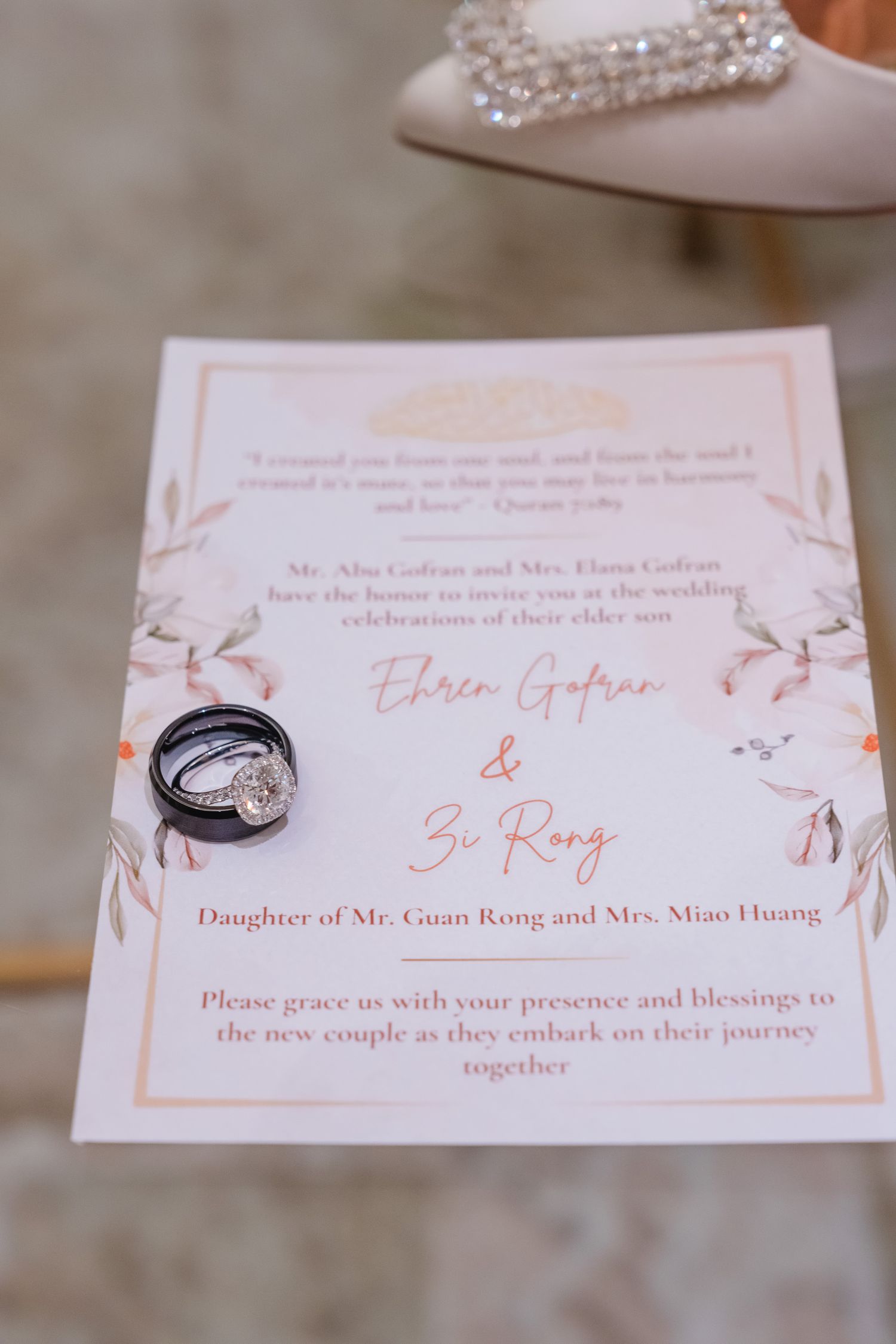 Wedding invitation with elegant floral design and wedding rings placed on top in soft lighting.
