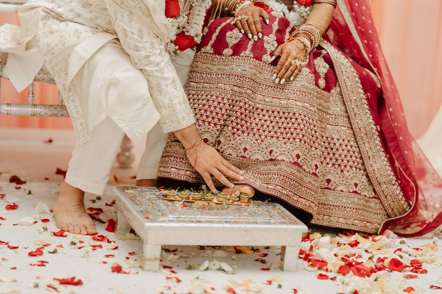 Traditional Indian wedding details showing ornate bridal attire and henna decorated hands with red rose petals.