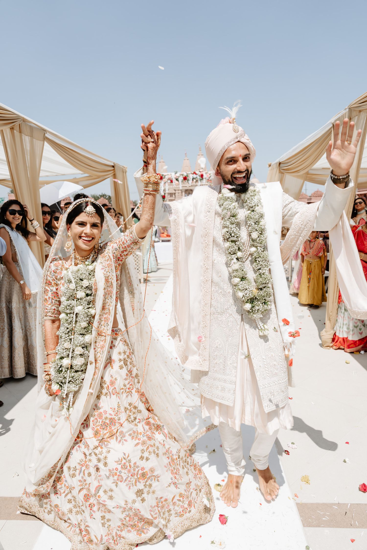Joyful wedding celebration with couple in traditional Indian attire under outdoor canopy.
