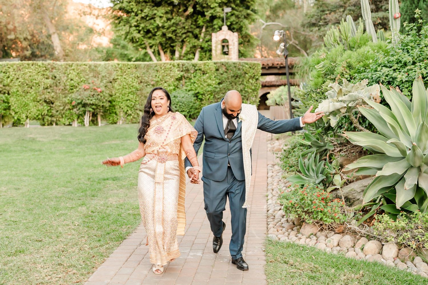 A couple walks joyfully through a lush garden path during their wedding celebration.