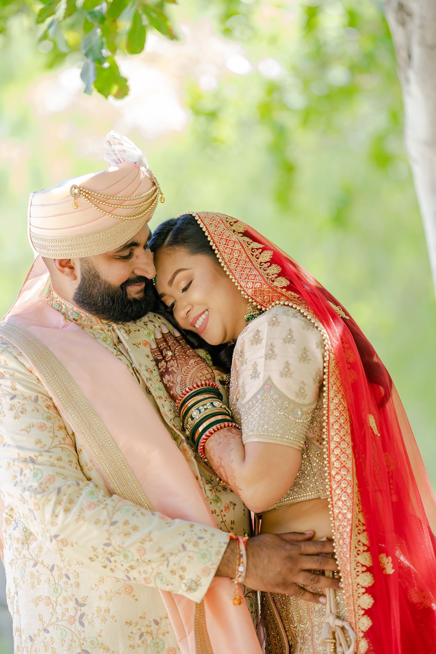 Couple in traditional Indian wedding outfits sharing intimate moments in a sunlit garden setting.
