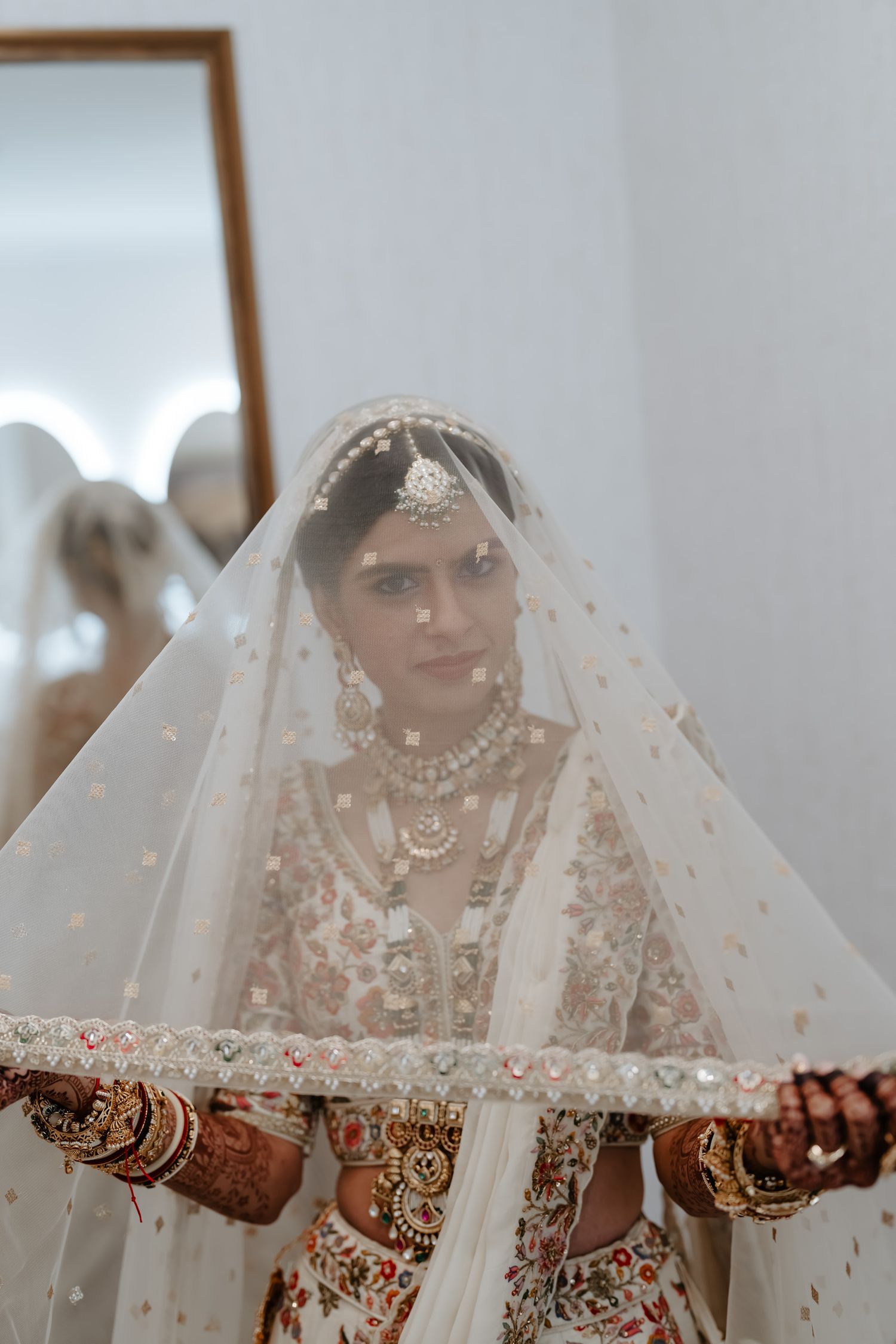 Traditional Indian bride in white veil and ornate jewelry shows decorated hands with henna.
