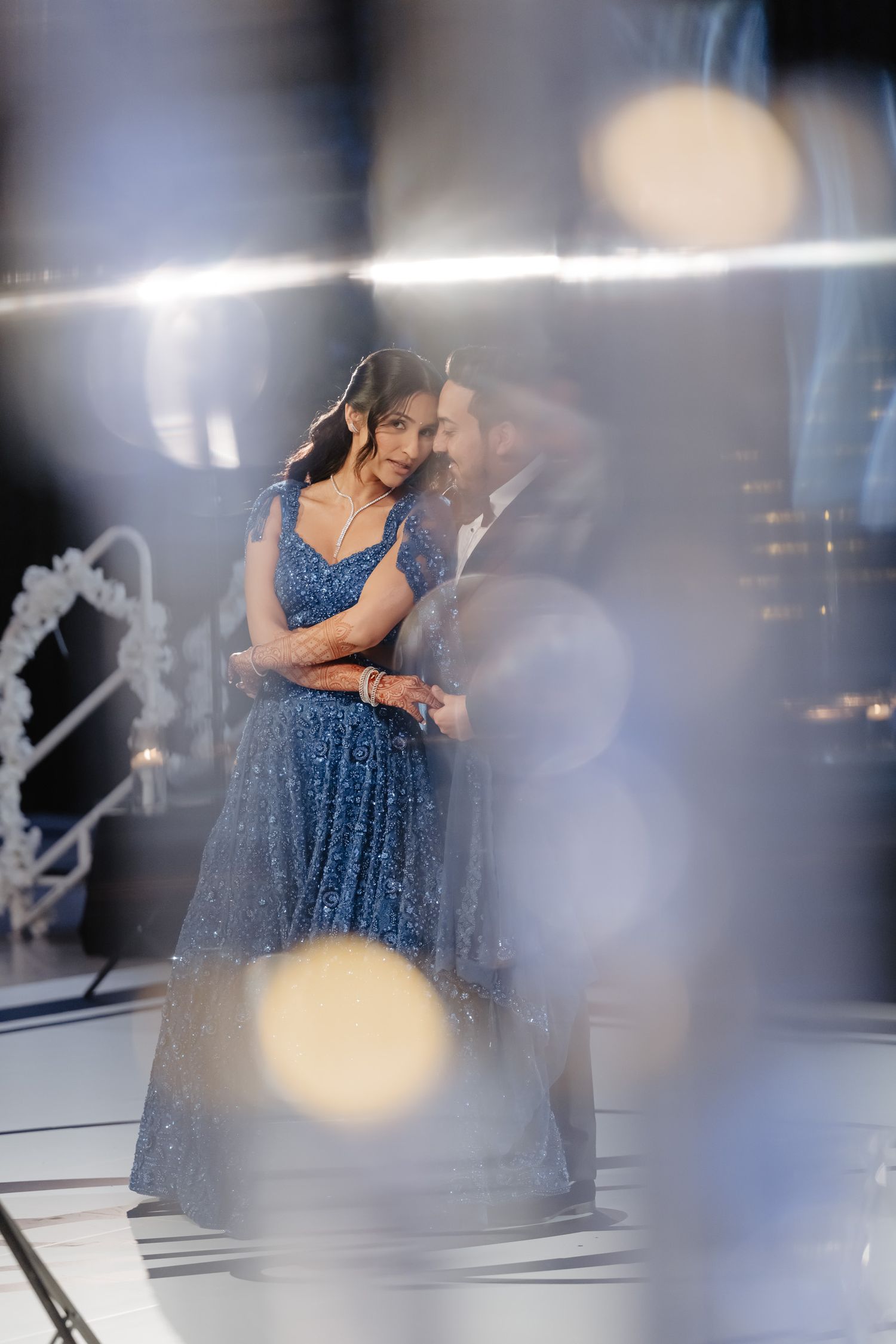 Woman in sparkly blue gown poses elegantly against dramatic lighting in a photo studio setting.