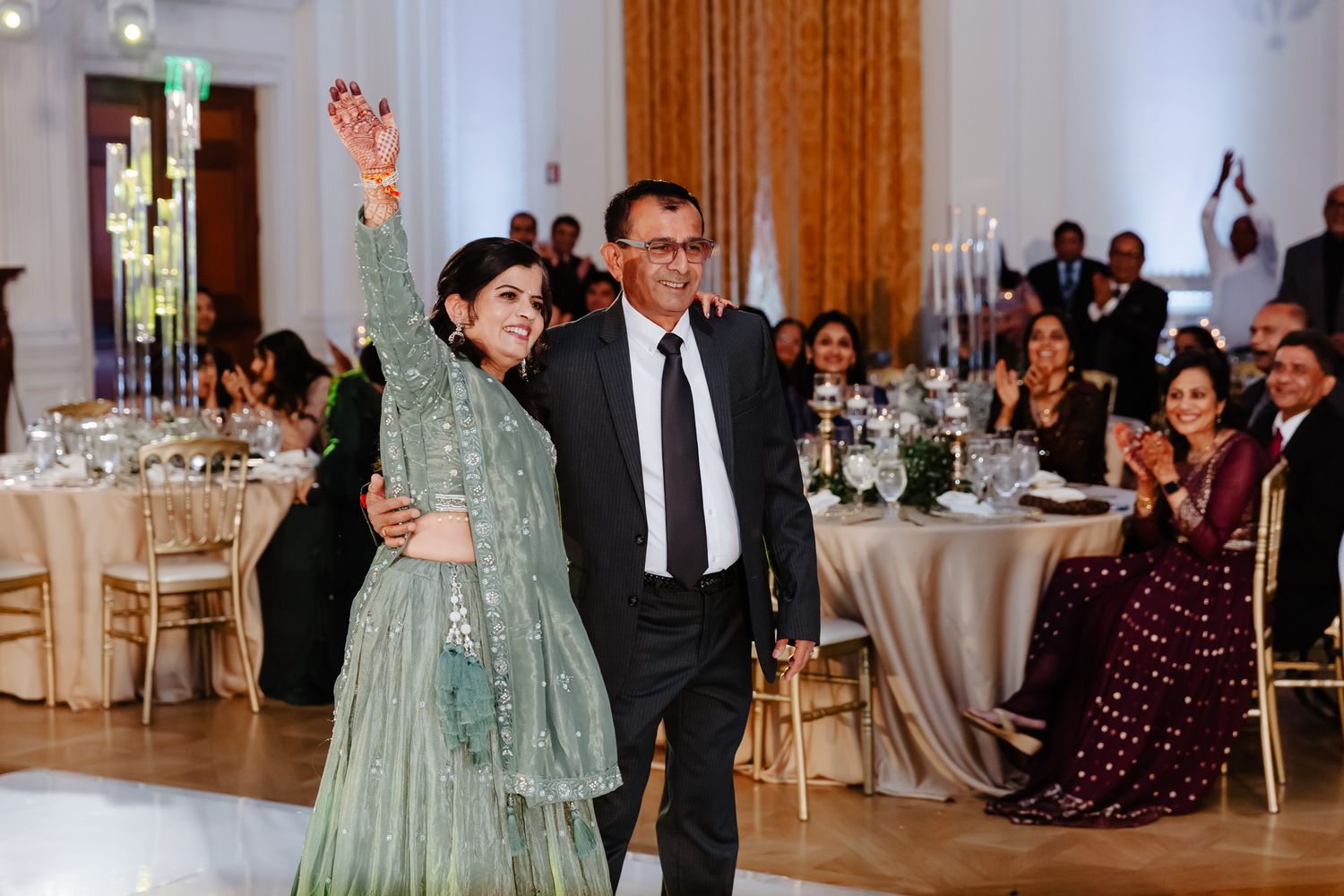 Elegant wedding reception venue with white tables, warm lighting, and guests enjoying the celebration.