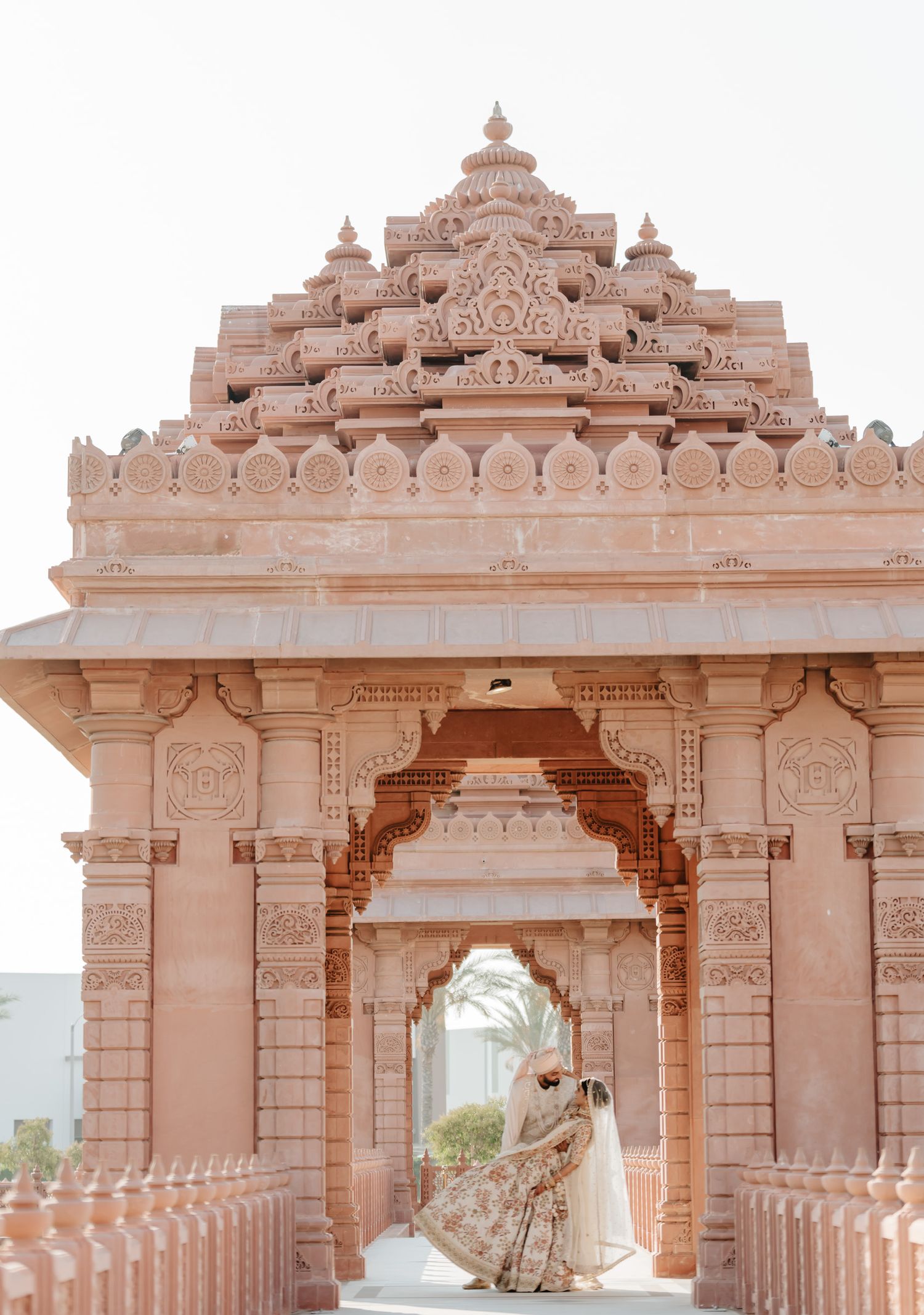 A grand ornate pink stone temple entrance with intricate architectural details frames a special moment.