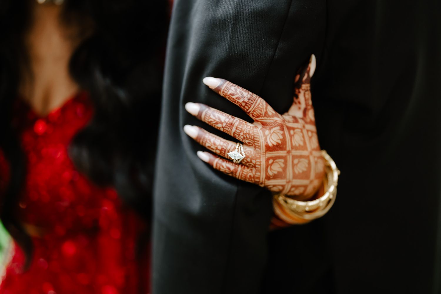 Close-up detail of intricate henna designs on hands with red fabric in background.