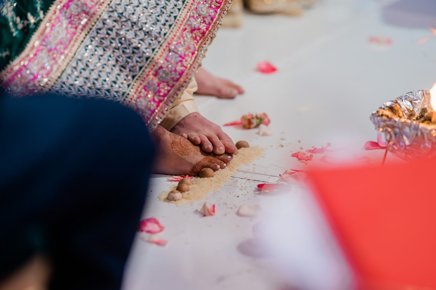 Close-up of feet and scattered rose petals on floor during traditional Indian wedding ceremony.
