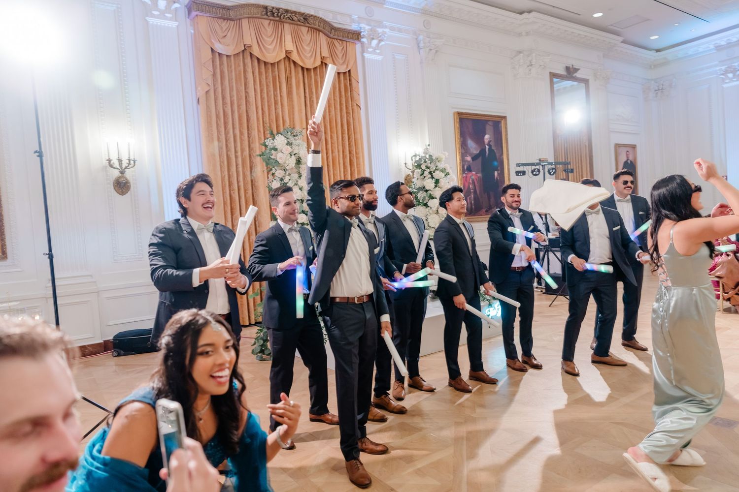 Wedding guests form a line on the dance floor during a reception celebration in an elegant ballroom.
