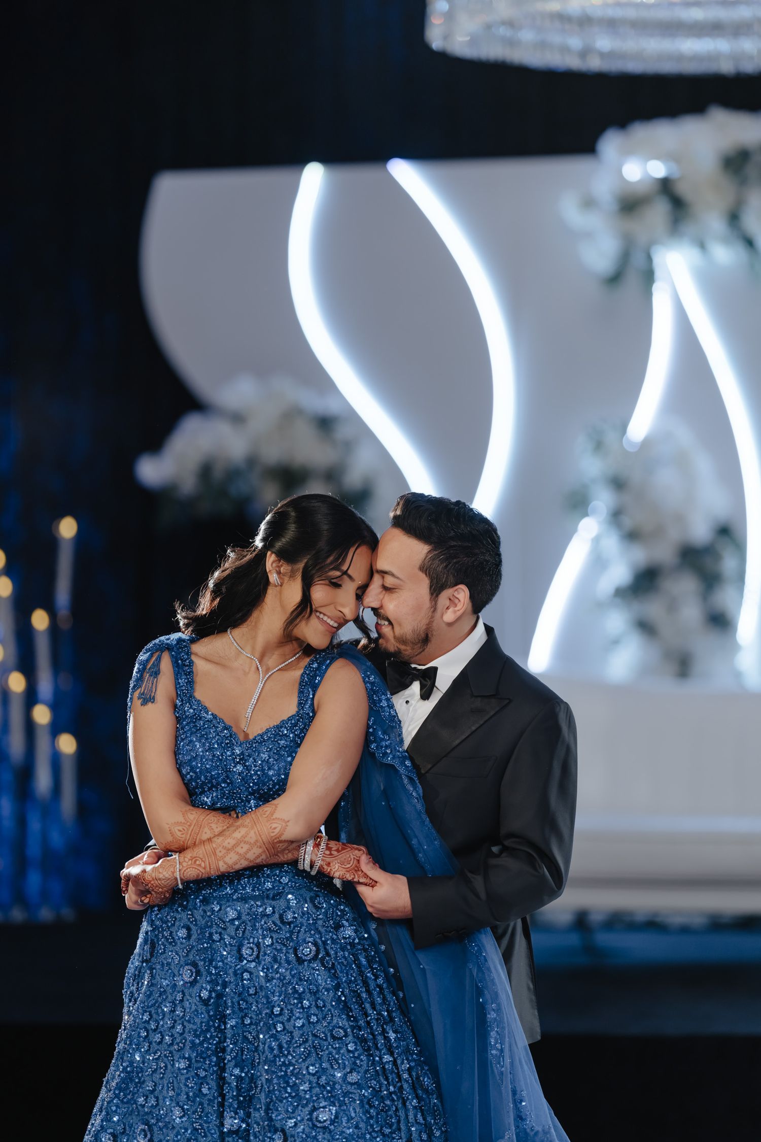 Romantic dance moment between couple with woman in sequined blue gown under ambient lighting.