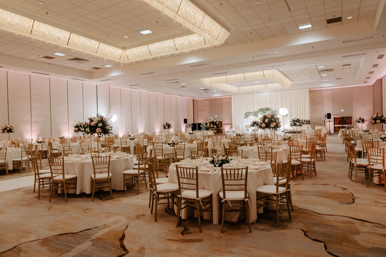 Elegant wedding reception ballroom with round tables, white linens, and warm lighting creating a sophisticated atmosphere.