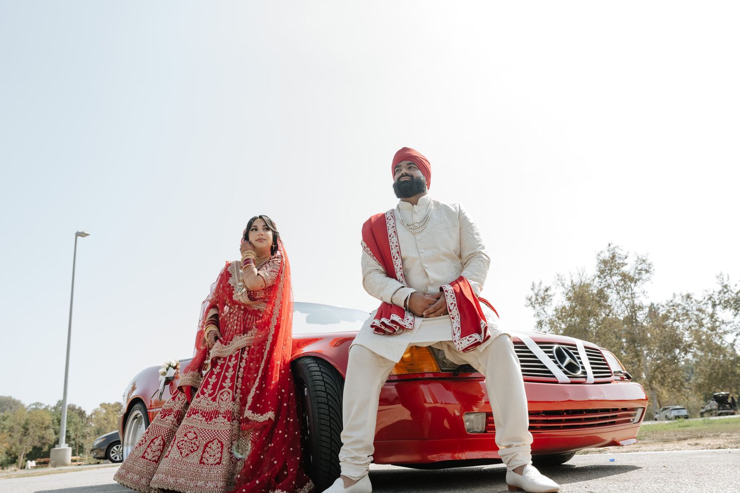 Red vintage convertible car parked outdoors during a traditional Indian wedding celebration.