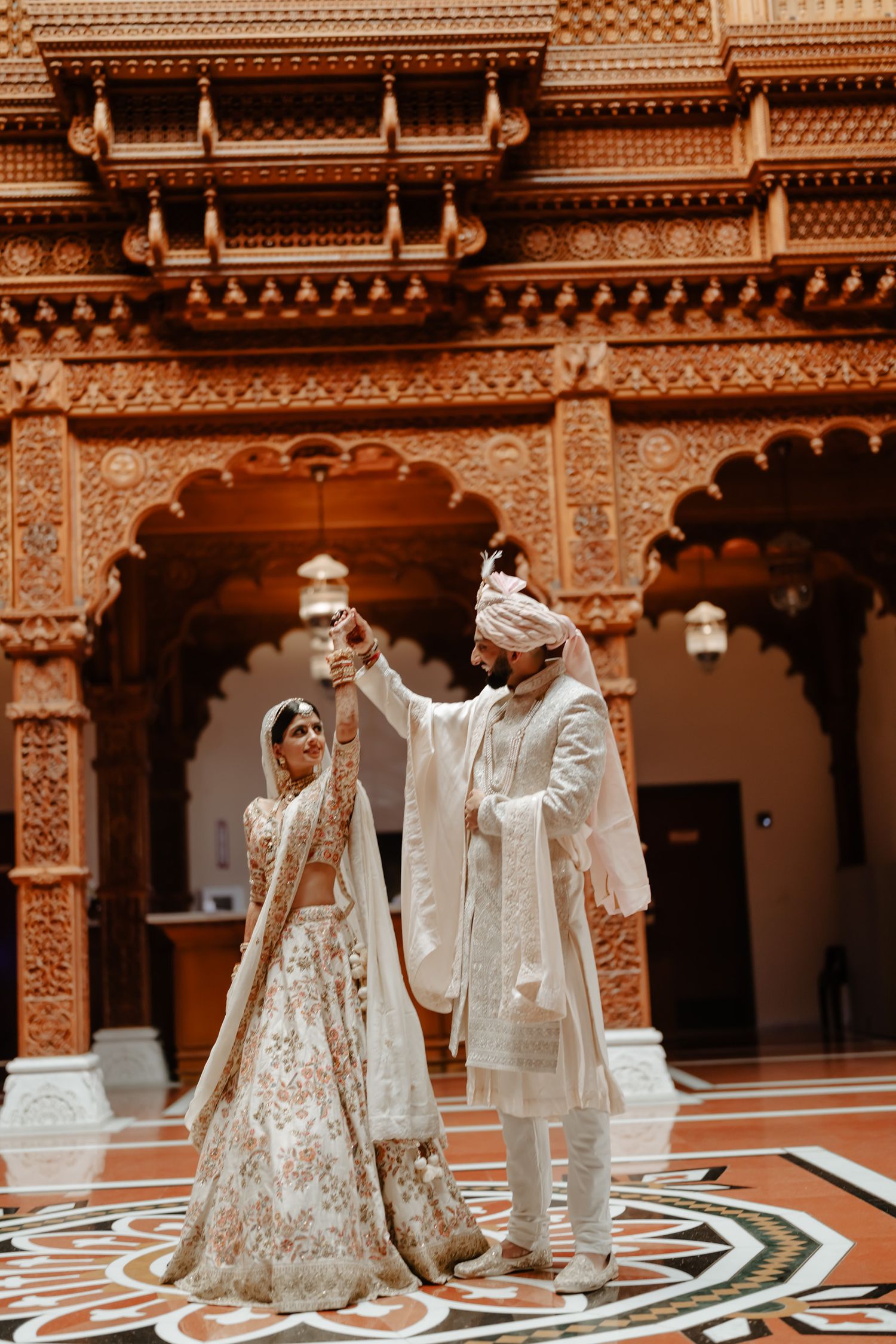 Traditional Indian wedding ceremony with couple in ornate white and gold outfits under intricately carved archways.