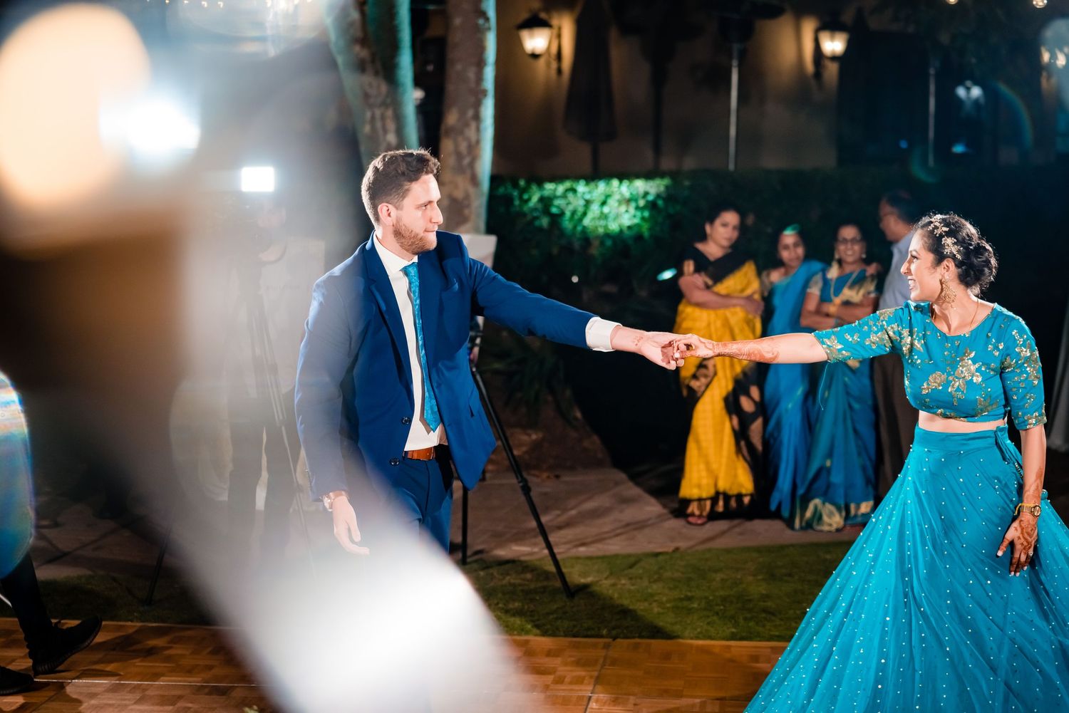 Couples dancing at an evening wedding reception with blue and yellow formal attire under outdoor lighting.