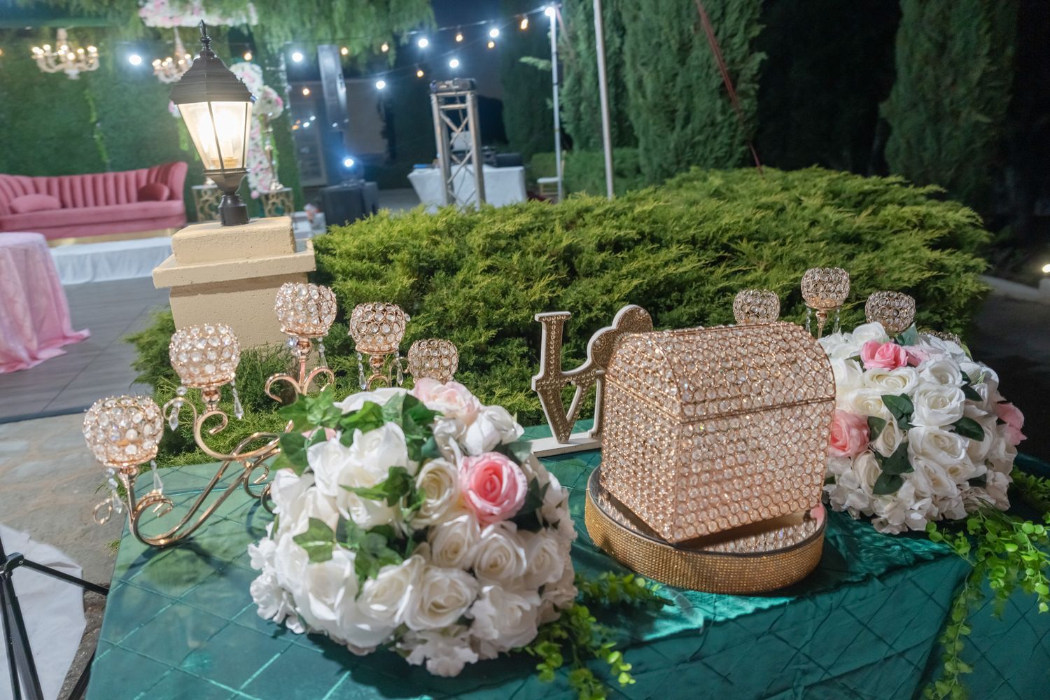 Elegant wedding dessert table with crystal chandeliers and floral decorations on turquoise tablecloth.