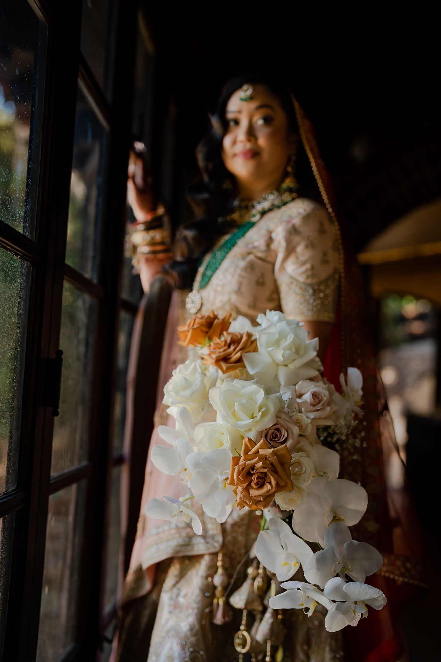 Beautiful bridal bouquet with white orchids and gold roses in foreground of traditional South Asian wedding attire.