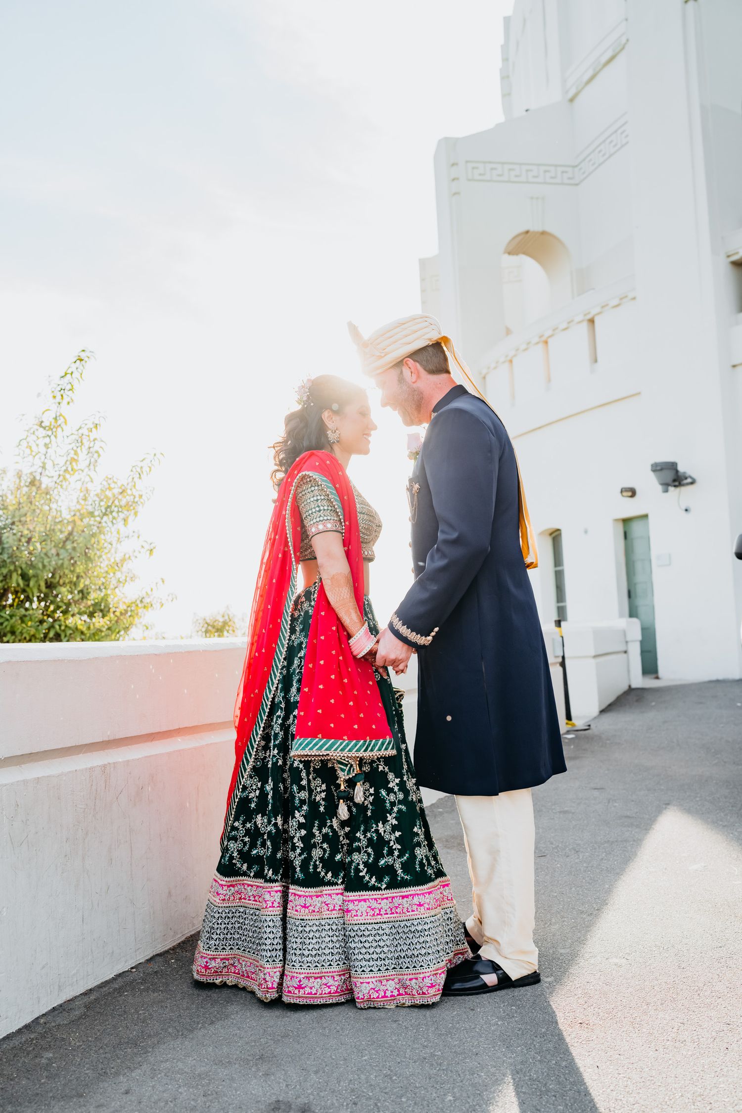 A couple in traditional wedding attire walks together against a white building exterior.