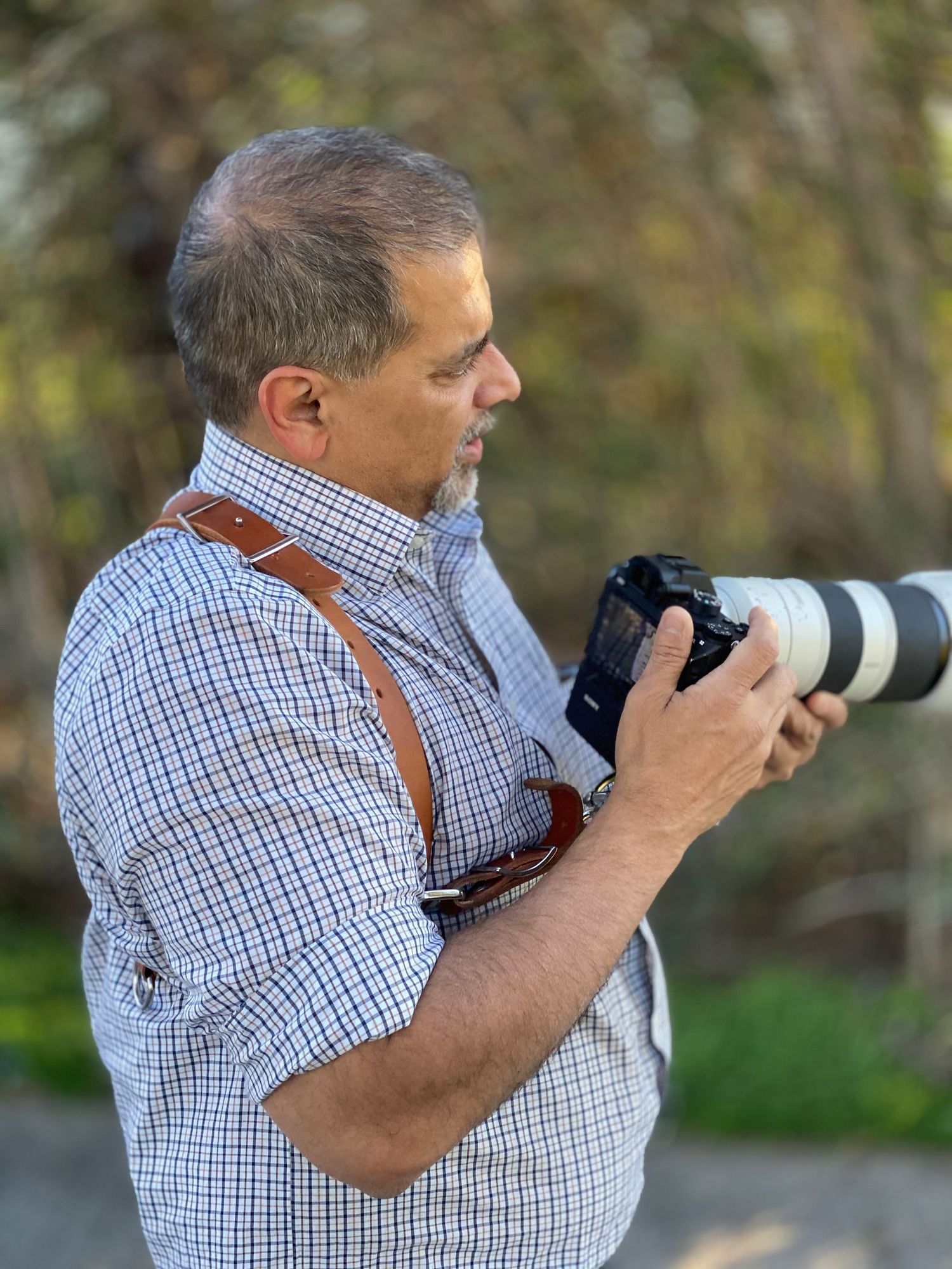 Photographer with telephoto lens camera and leather strap outdoors.