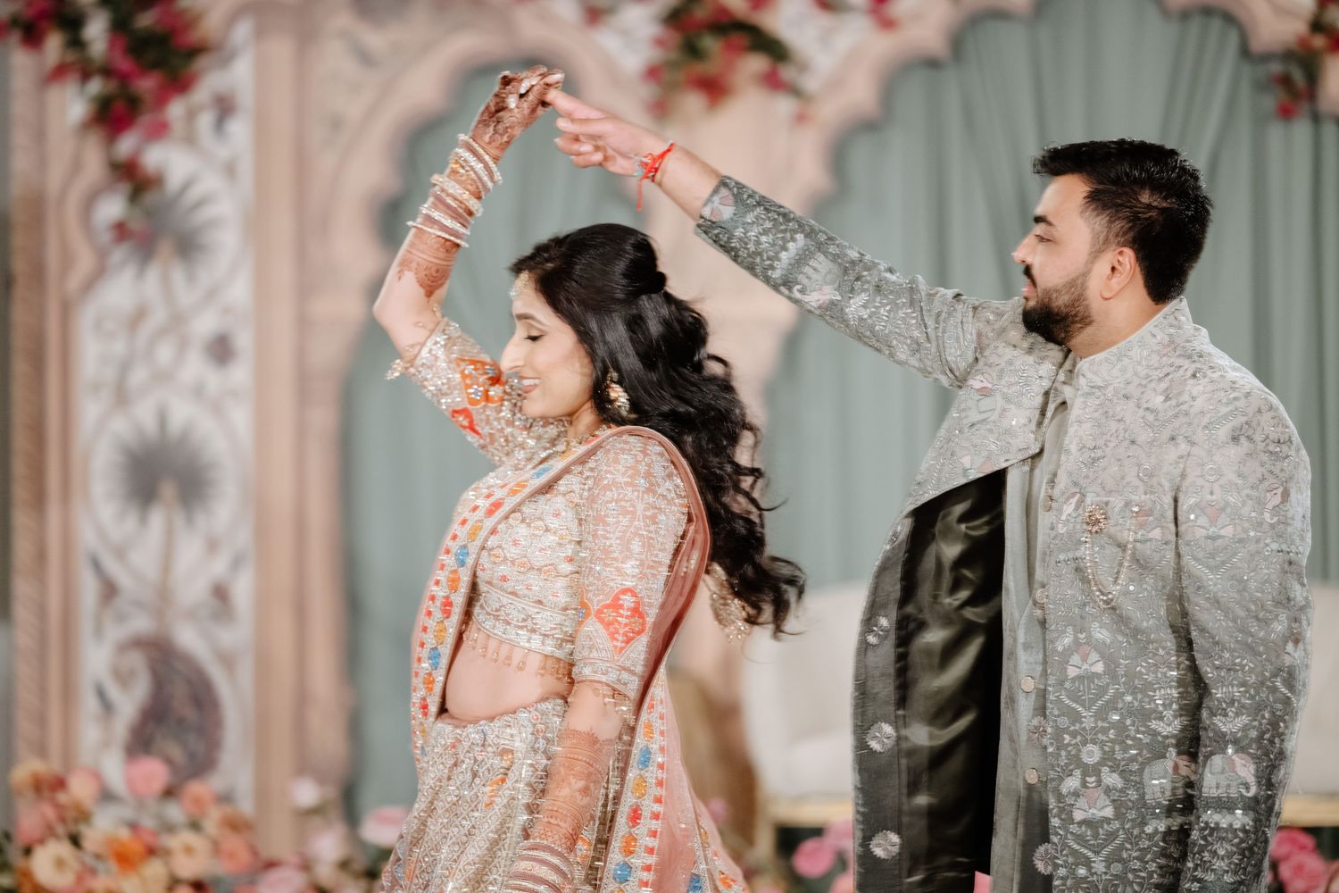 Couple in traditional Indian wedding attire, groom spinning bride in elegant lehenga at decorated ceremony venue.