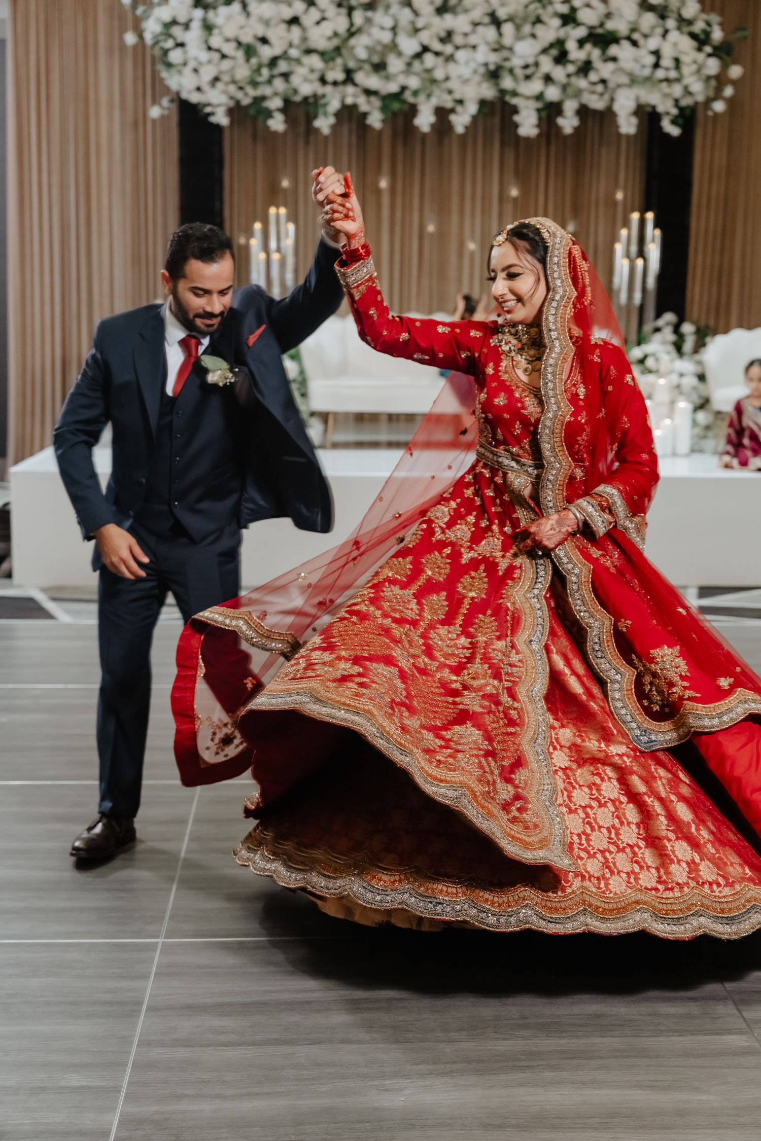 Wedding couple dances together as the bride's red lehenga swirls across the floor.