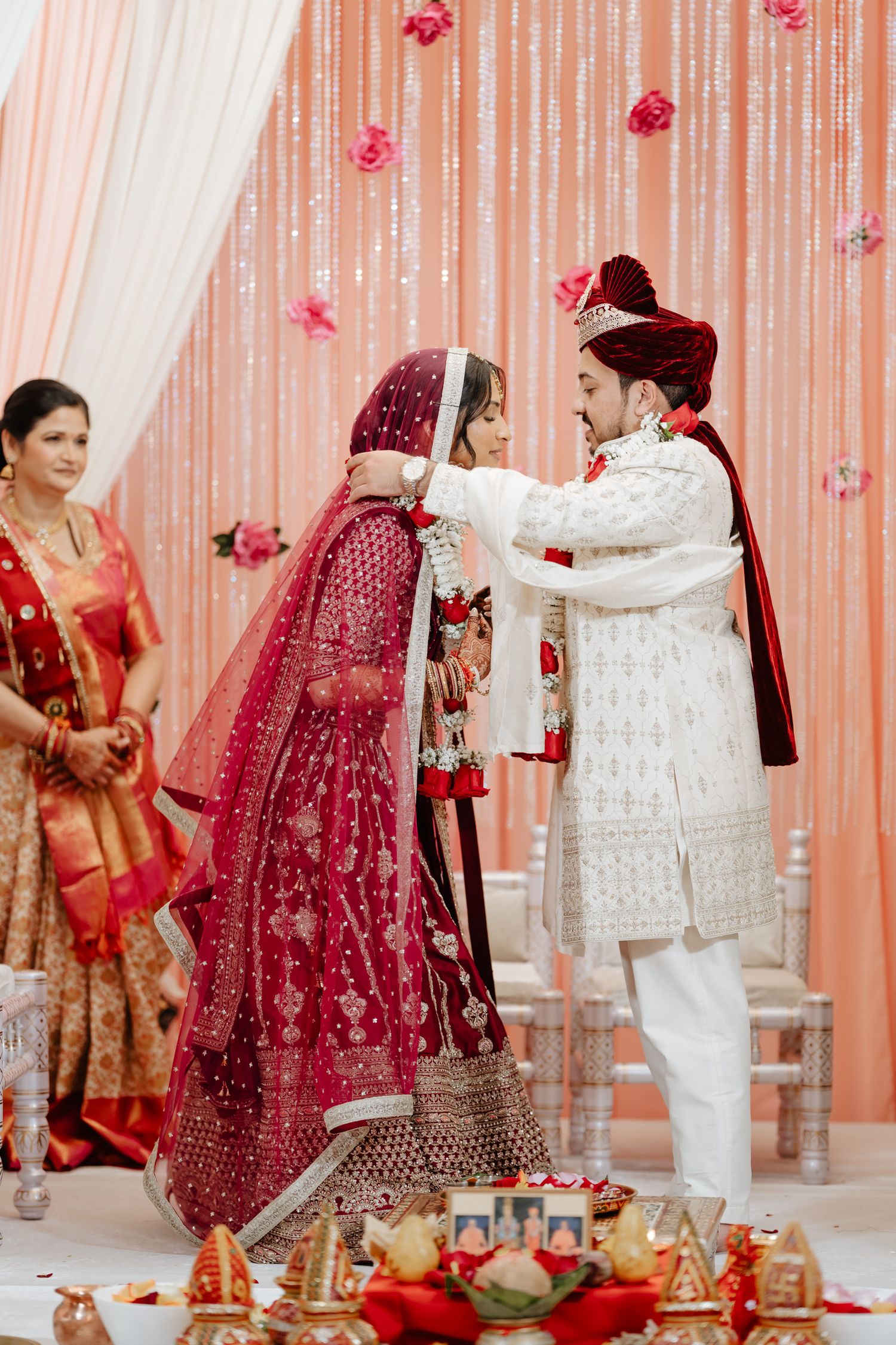 A traditional Indian wedding ceremony with a couple performing rituals under pink floral decorations.