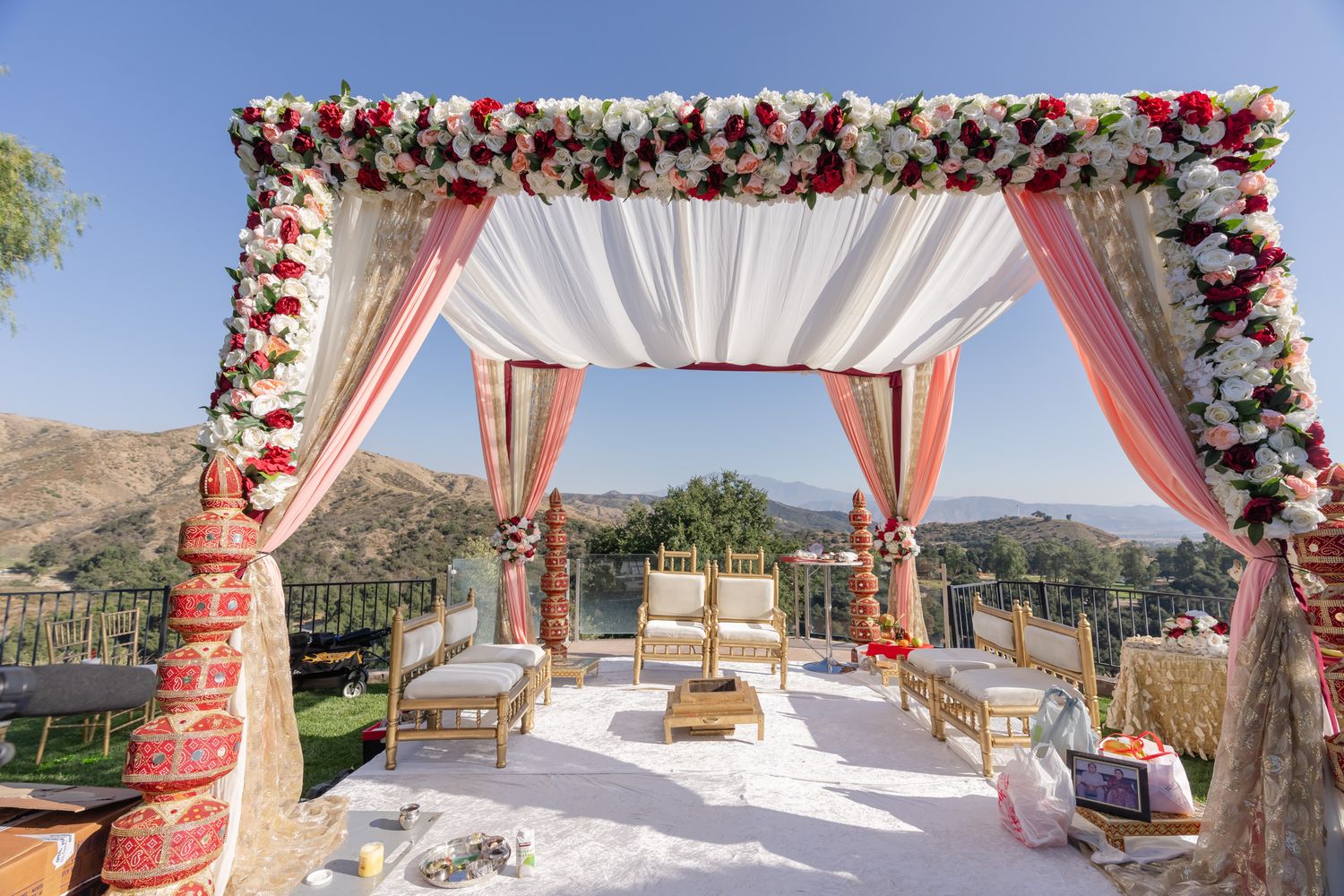 Outdoor wedding ceremony setup with white draped canopy and floral arch against a mountain backdrop.