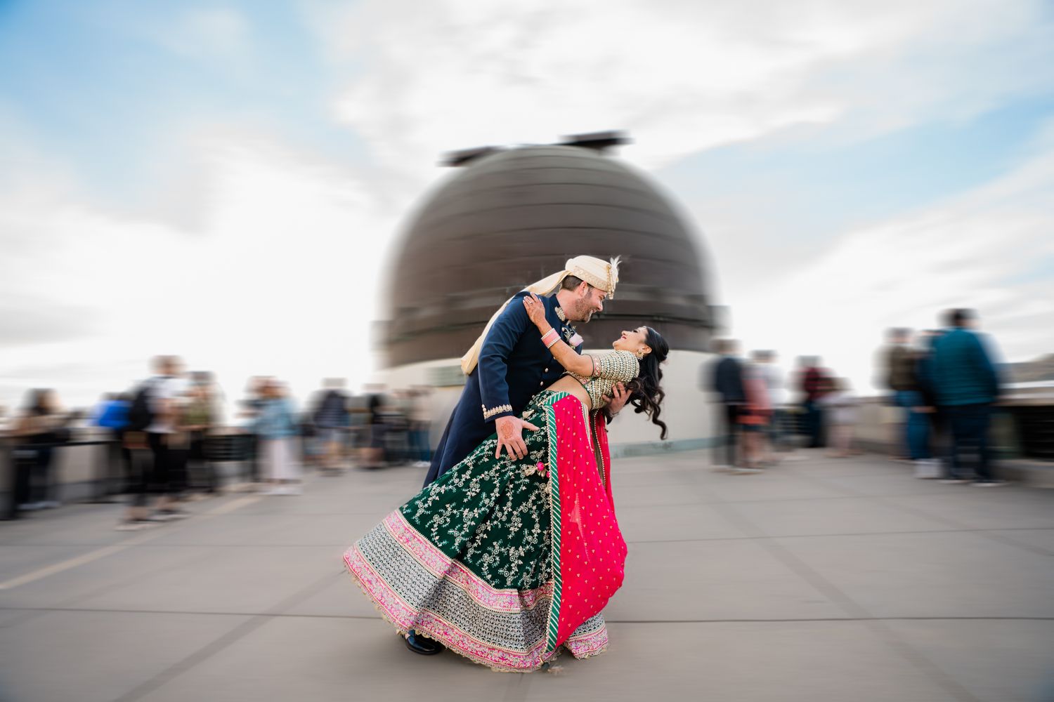 A couple in formal attire performs a romantic dip dance pose on a rooftop with a city skyline in the background.
