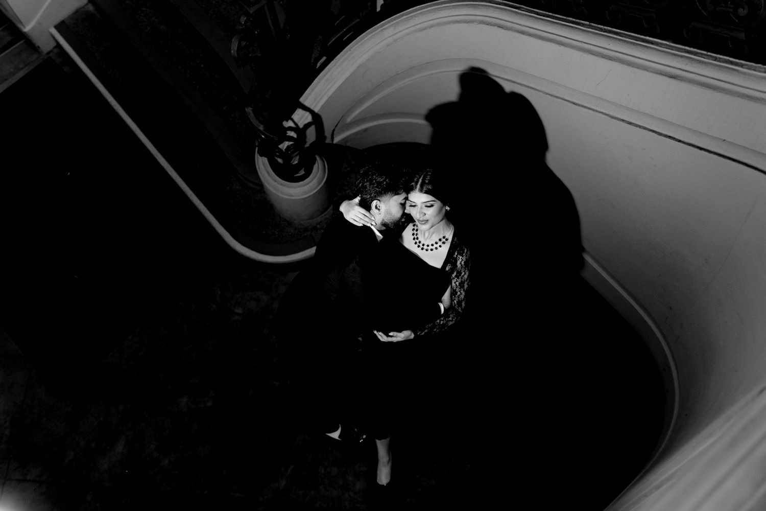 Black and white aerial shot of couple sharing intimate moment on ornate staircase.