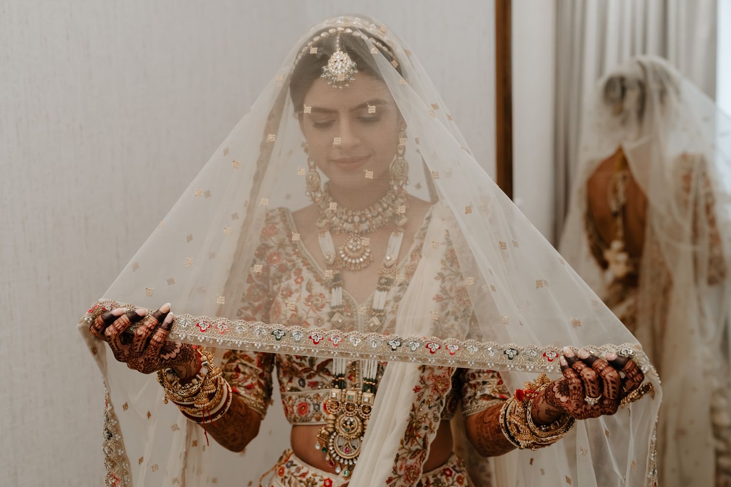 Close up of intricate henna designs and jewelry under sheer wedding veil.