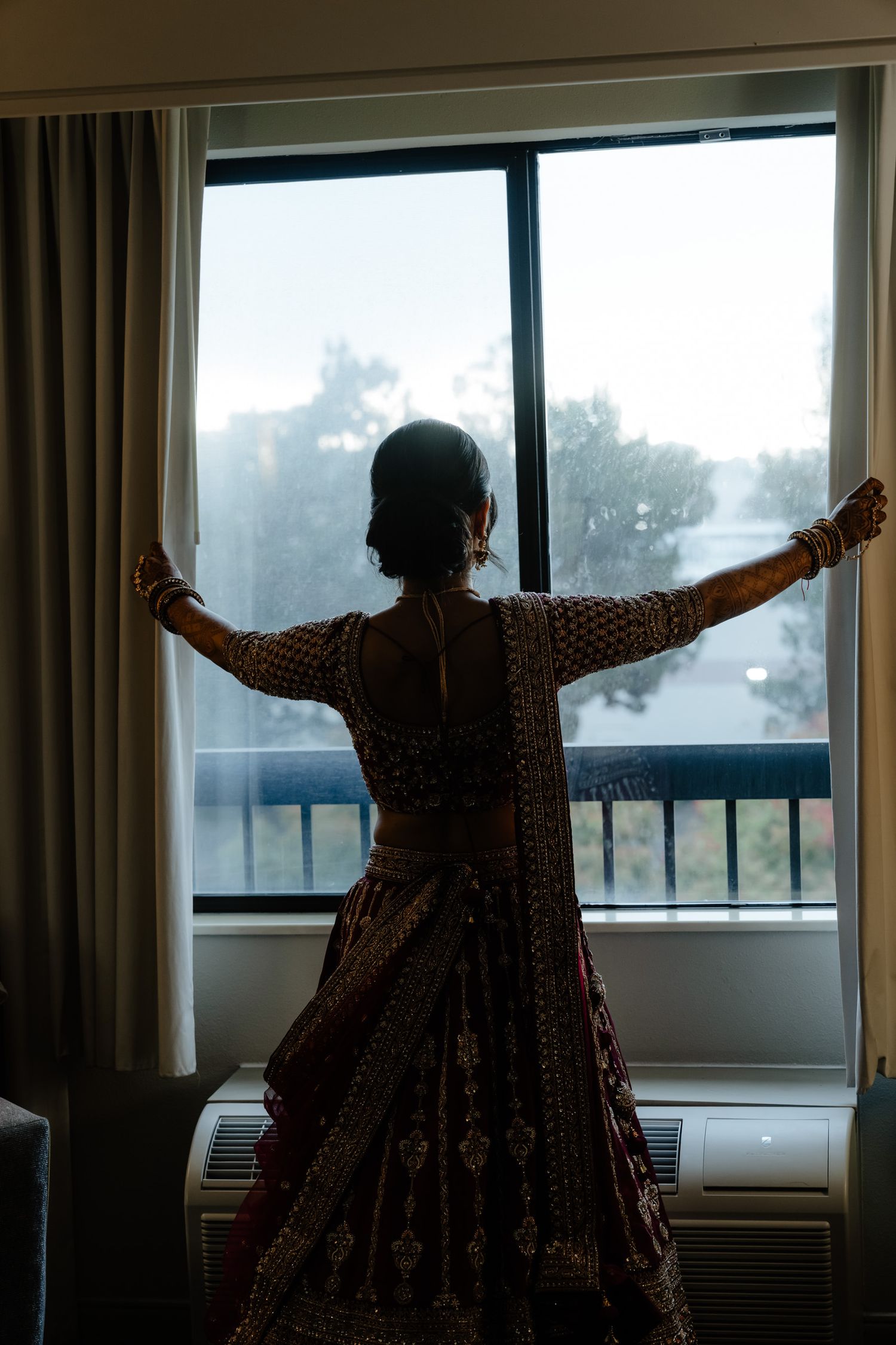 Silhouetted figure stretches arms wide in front of sunlit hotel room window in dramatic pose.